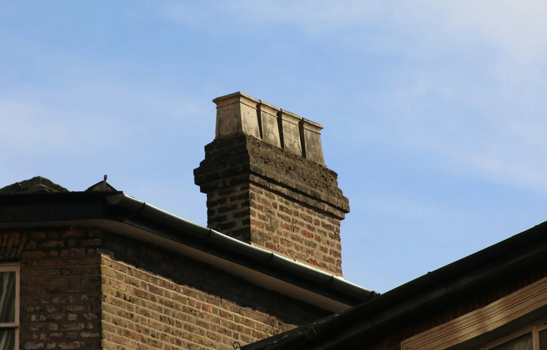 Brick house with a chimney stack and dark fascia boards and gutters along the eaves