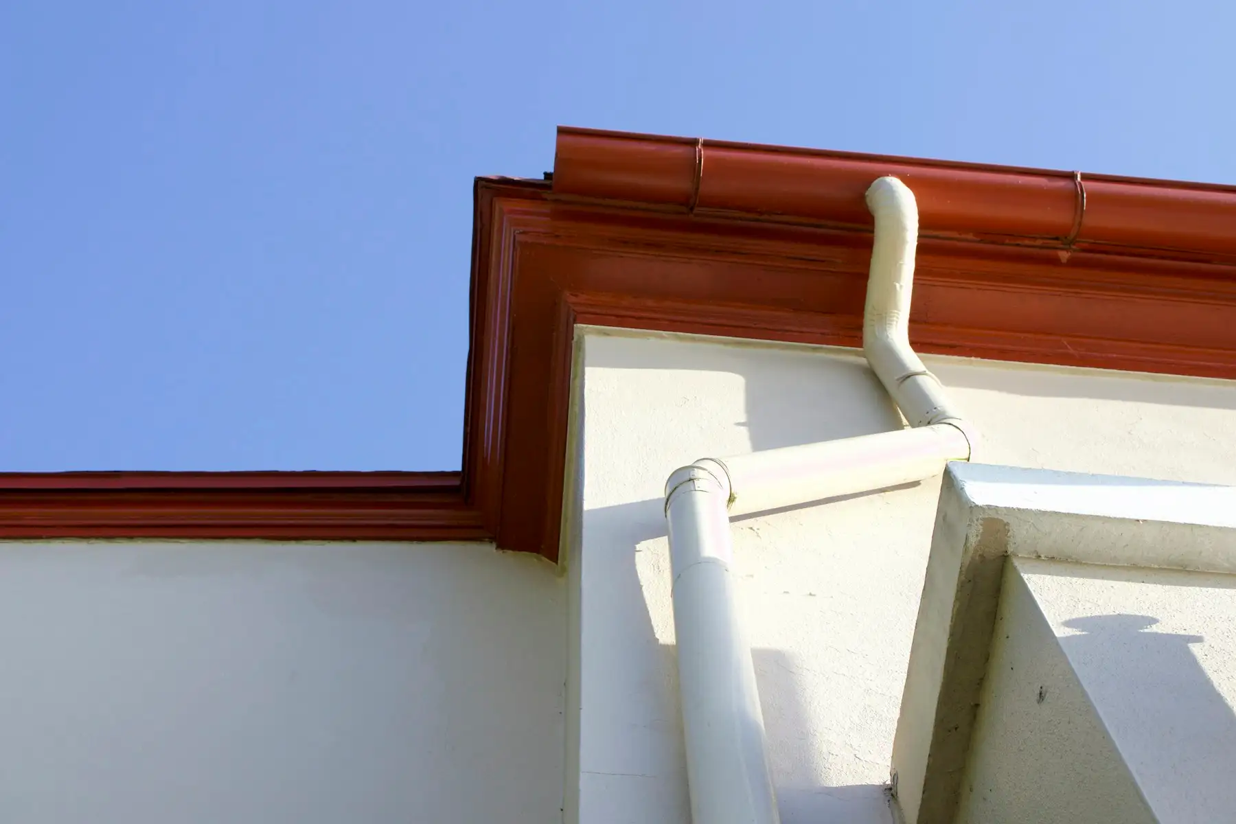 A red-brown gutter along white-rendered eaves with a white downpipe