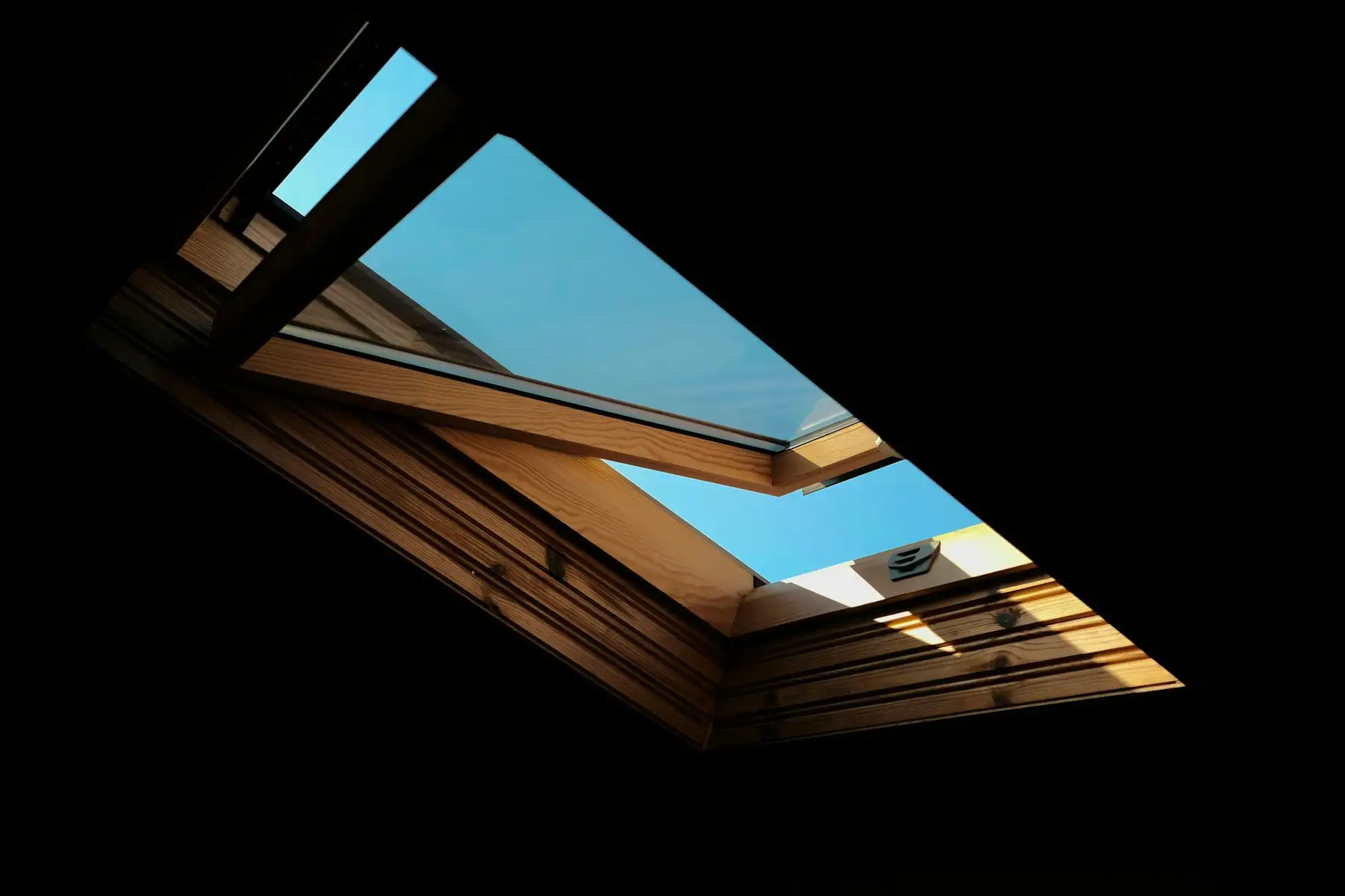 An open roof window seen from inside, with blue sky through the glass