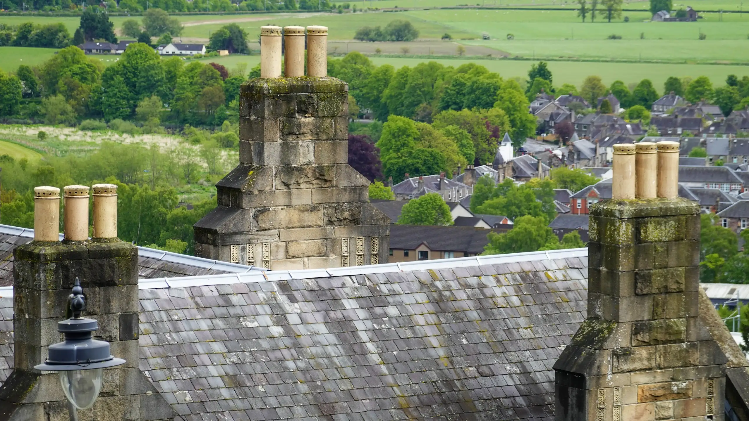 Slate roofs and stone chimney stacks looking out over a town and green fields