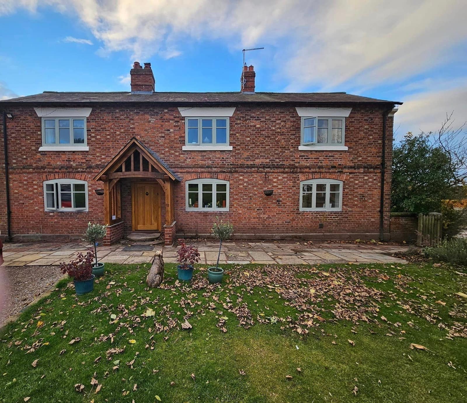 A double-fronted red-brick farmhouse with white window frames and an oak-framed porch, in low evening light