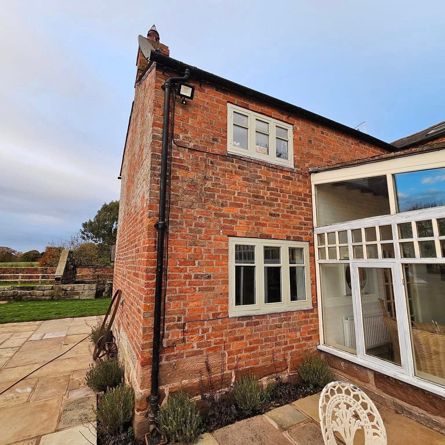 The gable end of a red-brick farmhouse beside a white conservatory, under a blue sky