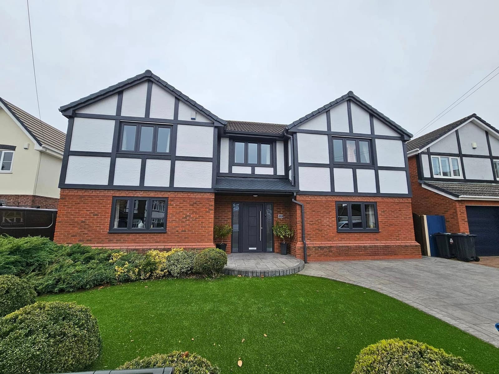 A detached mock-Tudor house with crisp black timbers on white gables above red brick, dark grey windows and a front lawn