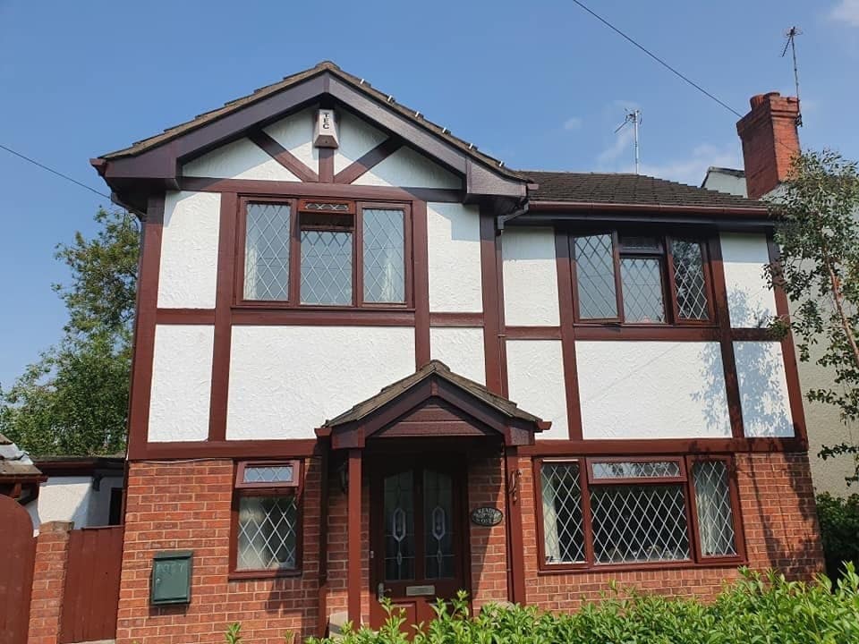 A mock-Tudor detached house with dark red timbers on white render above red brick and a gabled porch