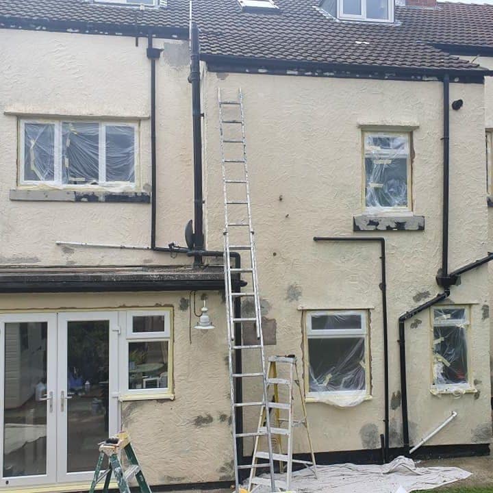 A rendered rear elevation mid-job: every window masked in plastic, repairs patched into the render, ladders up and the ground sheeted