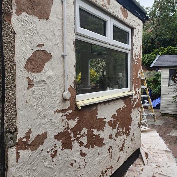 A textured rendered wall beside a window with large repairs patched in, before coating