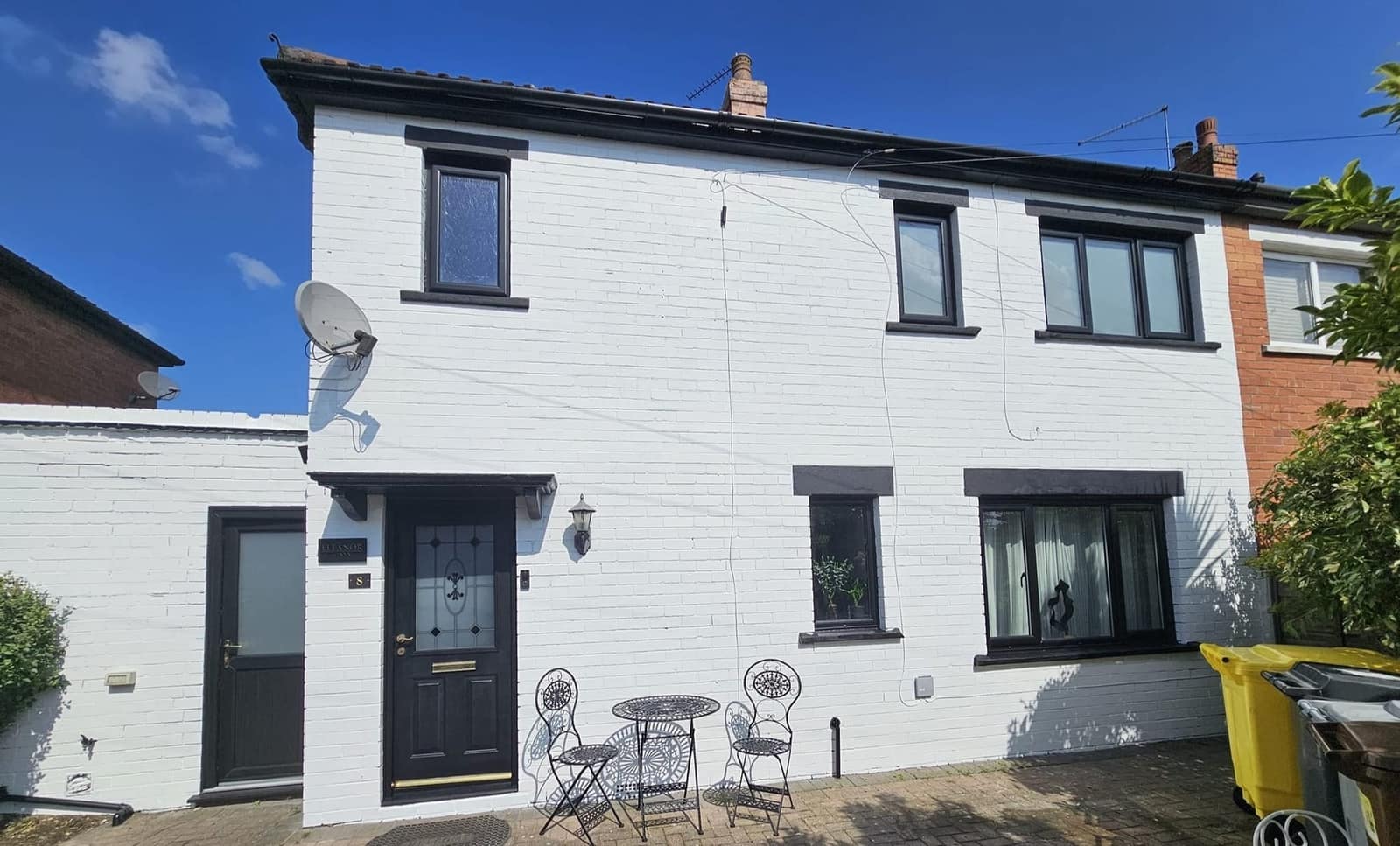 A semi-detached house with its brickwork painted white, grey window surrounds and a black front door, under a blue sky