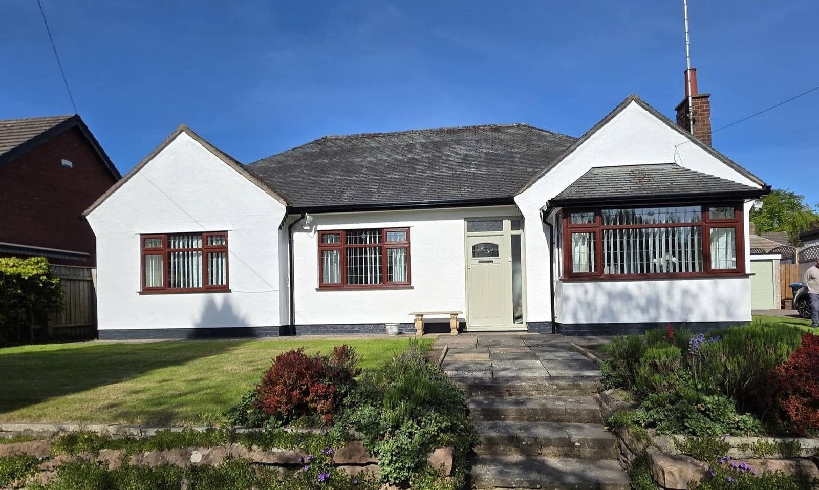 A white-painted bungalow with two bay windows and a sage green front door, behind a planted front garden