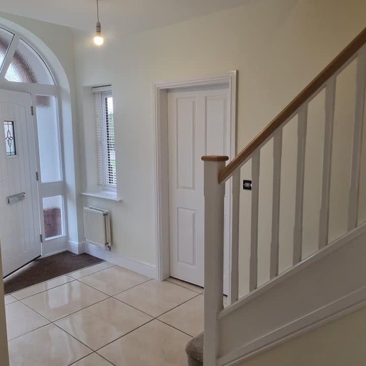 A bright entrance hall with an arched window over the front door, a white staircase and a tiled floor