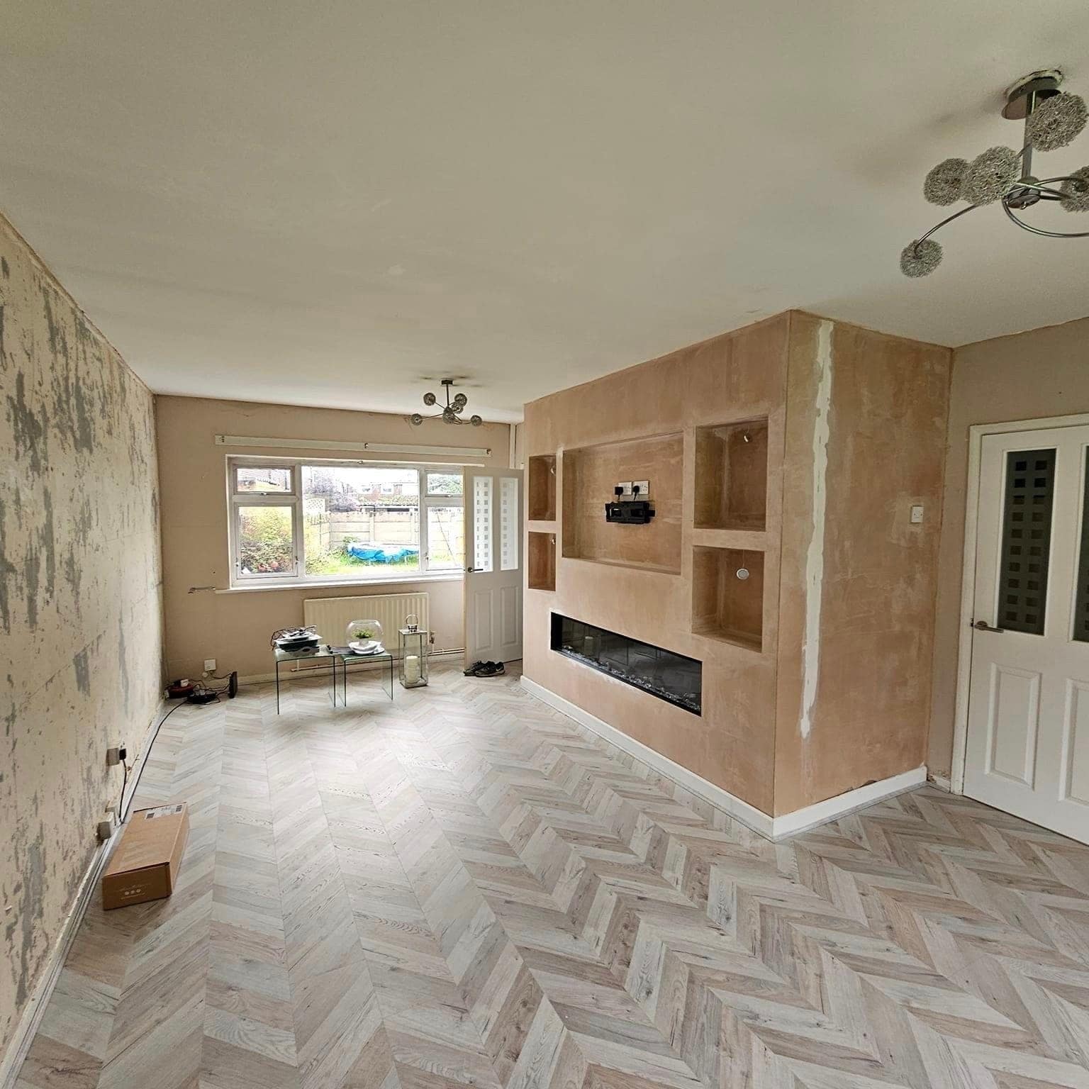 A living room part-way through: walls stripped back and a new chimney wall with shelving alcoves ready to decorate