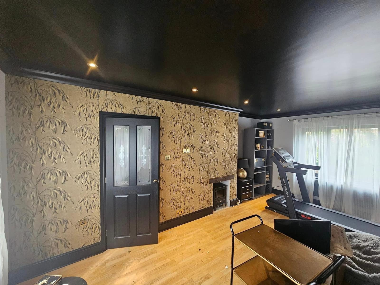 A gold-papered room under a black ceiling, with a black door and a home gym at the far end