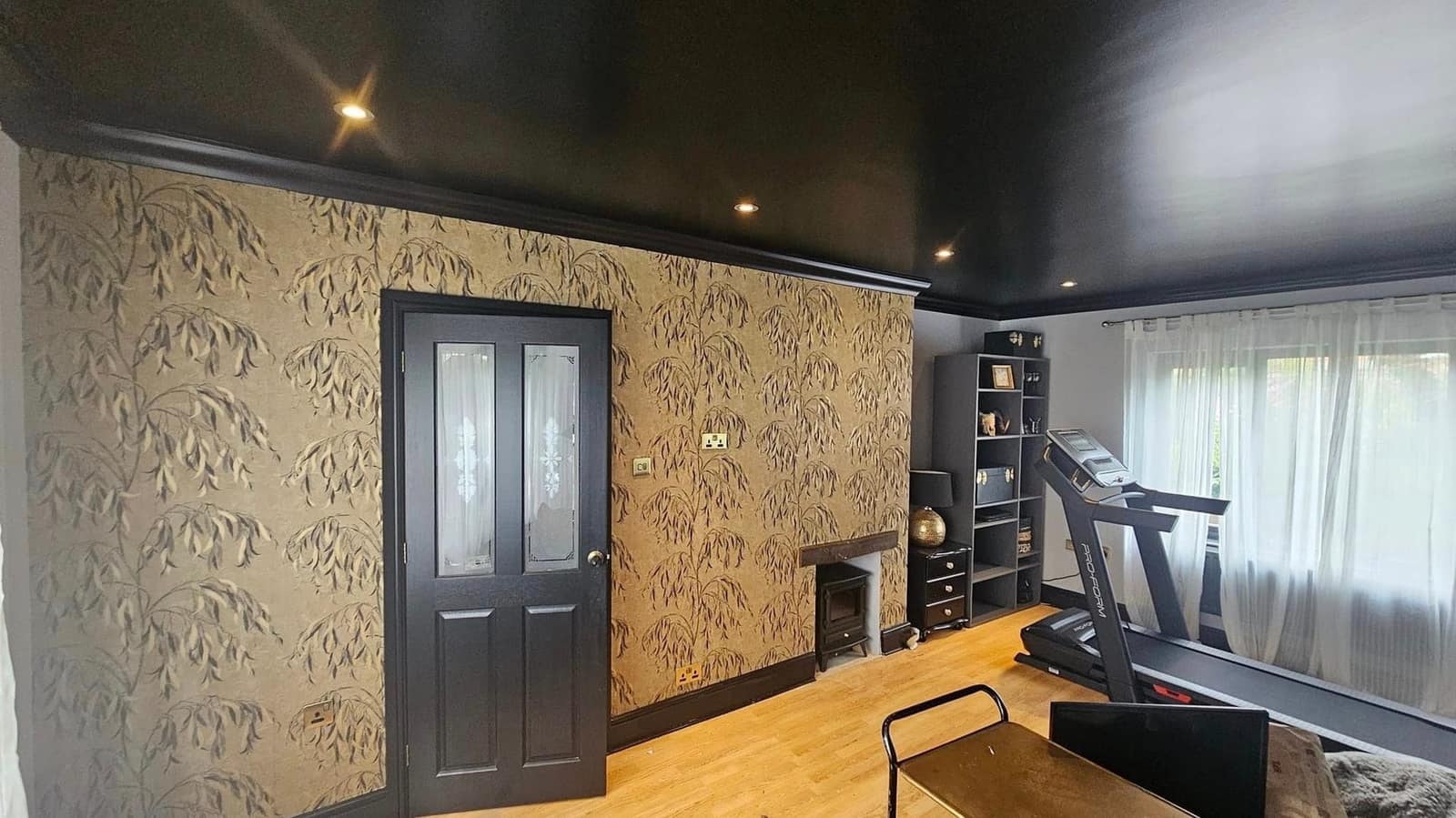 A room with a gold leaf-pattern paper on the walls, a black ceiling with downlights and a black four-panel door