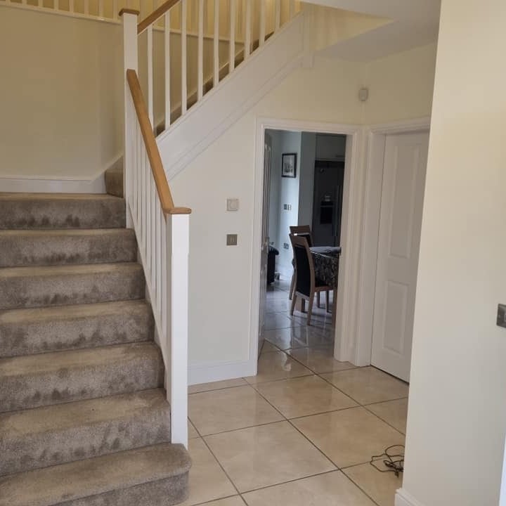 A hall and staircase with white spindles and an oak handrail, looking through to the kitchen