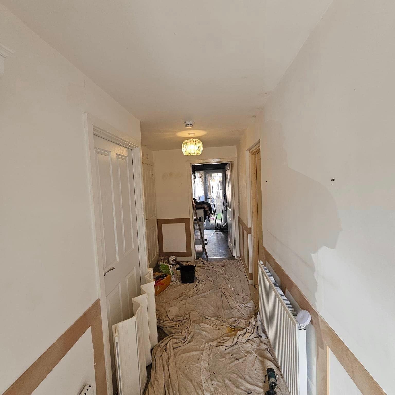 A hallway during preparation: floor sheeted end to end, walls filled and ready for paint