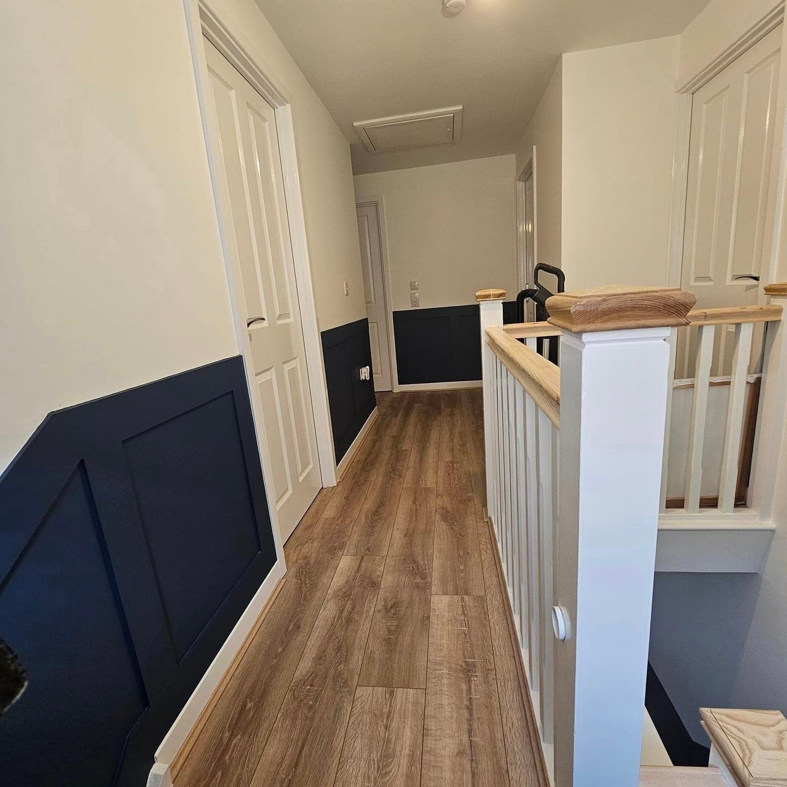 A landing with navy-painted panelling beneath a white balustrade and oak handrail, and wood flooring