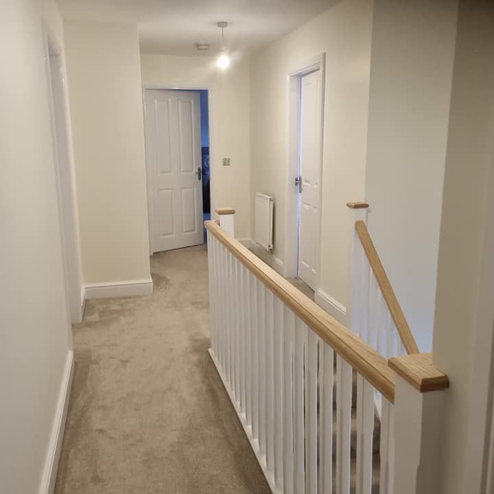 A landing with white spindles, an oak handrail and white doors