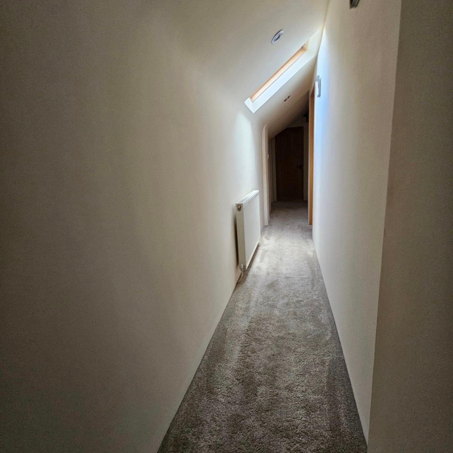 A long, narrow hallway painted white under a roof light, with a fresh carpet