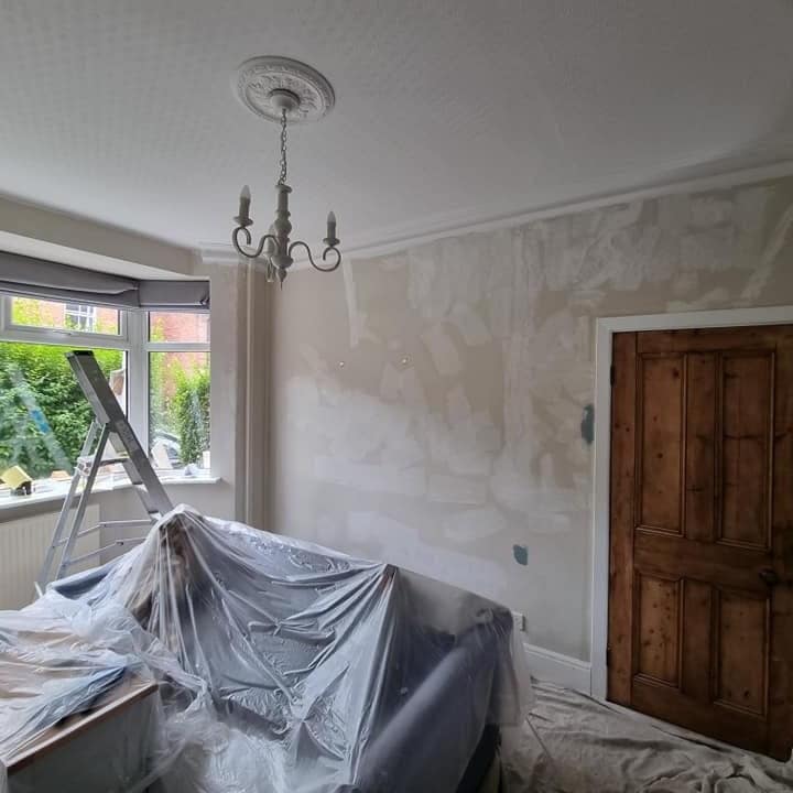 A lounge mid-job: the sofa wrapped in plastic, the floor sheeted and the walls made good before painting