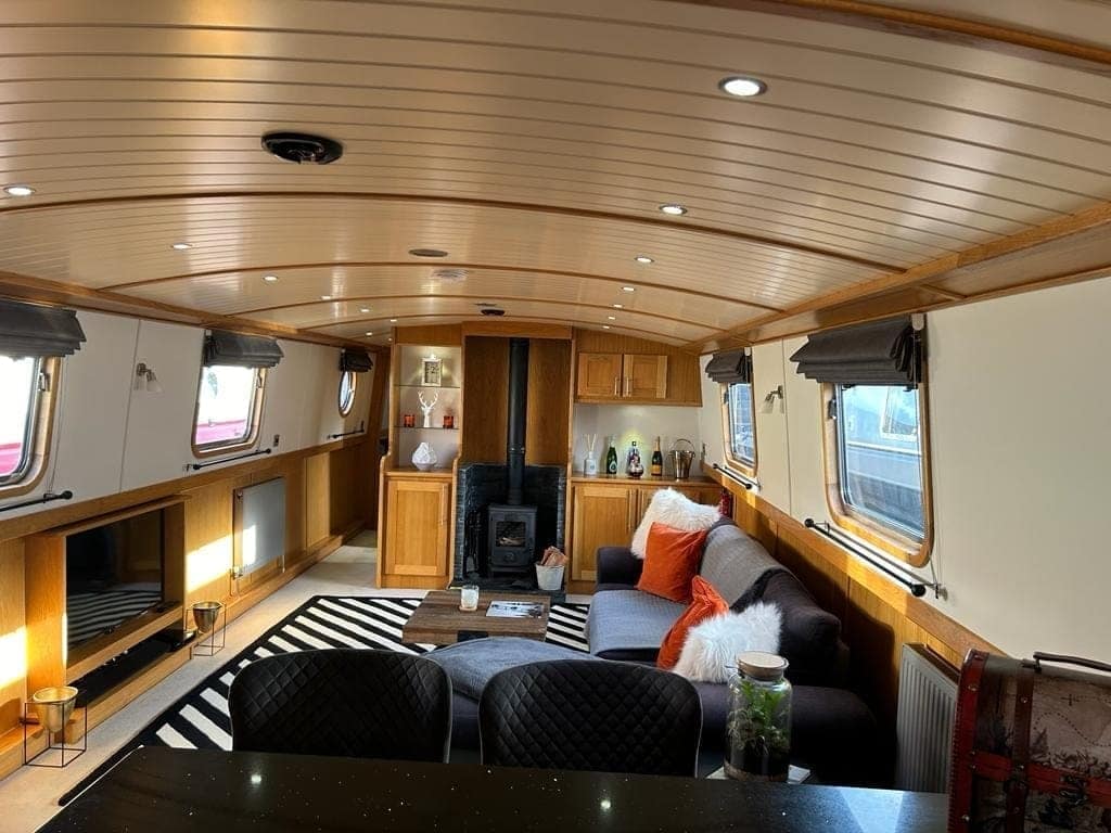 The inside of a narrowboat: a curved timber-clad ceiling, cream walls and a wood burner
