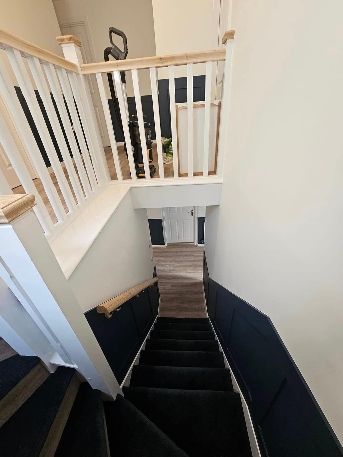 A staircase seen from the landing: white spindles, an oak handrail and bright white walls down to the hall