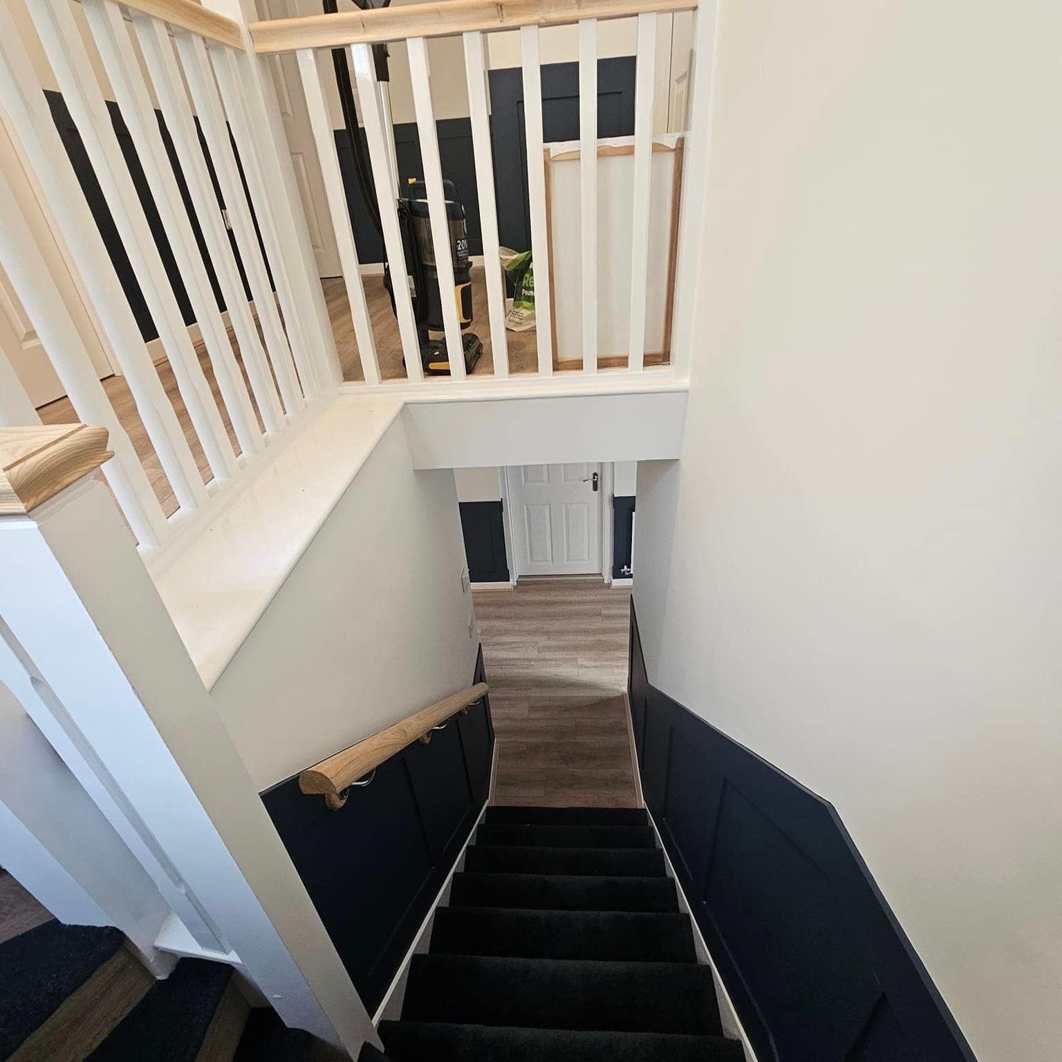 A staircase seen from the landing: white spindles and an oak rail above navy-painted panelling down both sides