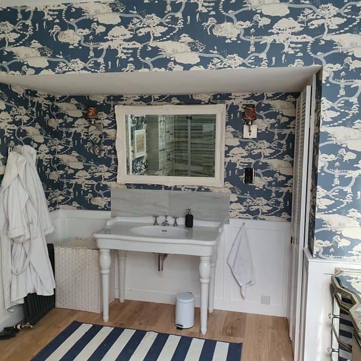 A washstand and mirror against white panelling, with the navy bird-print paper above it