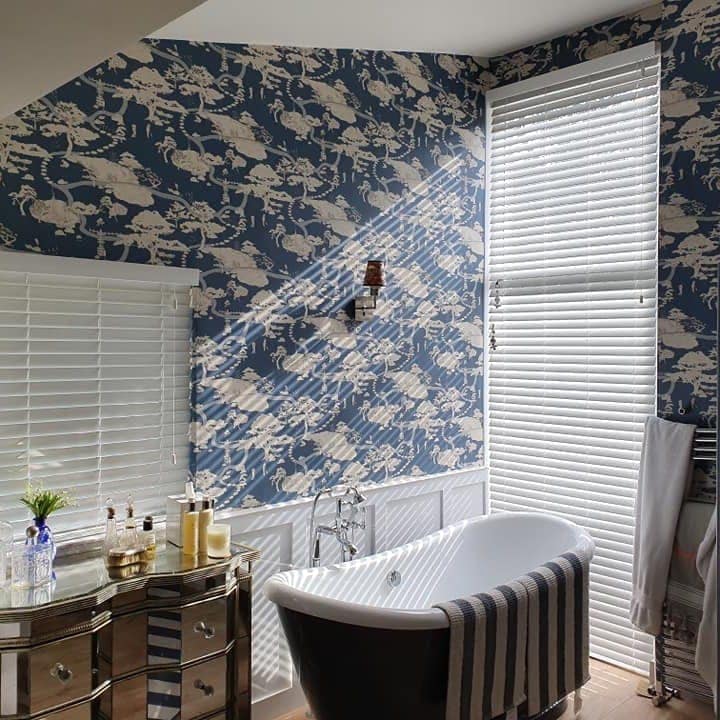 A bathroom papered in a navy print of white birds, with a black roll-top bath beneath a tall window