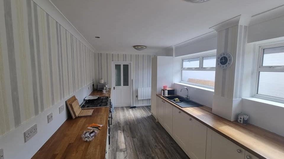 A long galley kitchen with a soft vertical-striped paper above the worktops