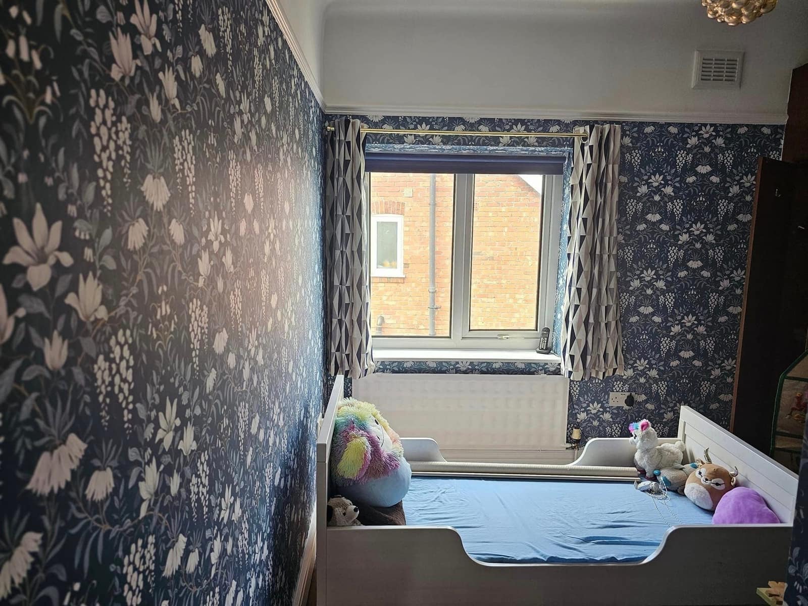 A child's bedroom papered in a navy floral print with matching curtains at the window