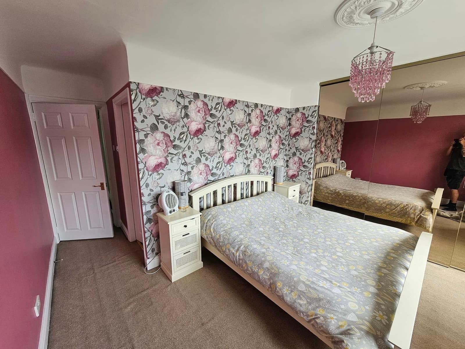 A bedroom with a large pink floral paper on the feature wall behind the bed and raspberry walls either side
