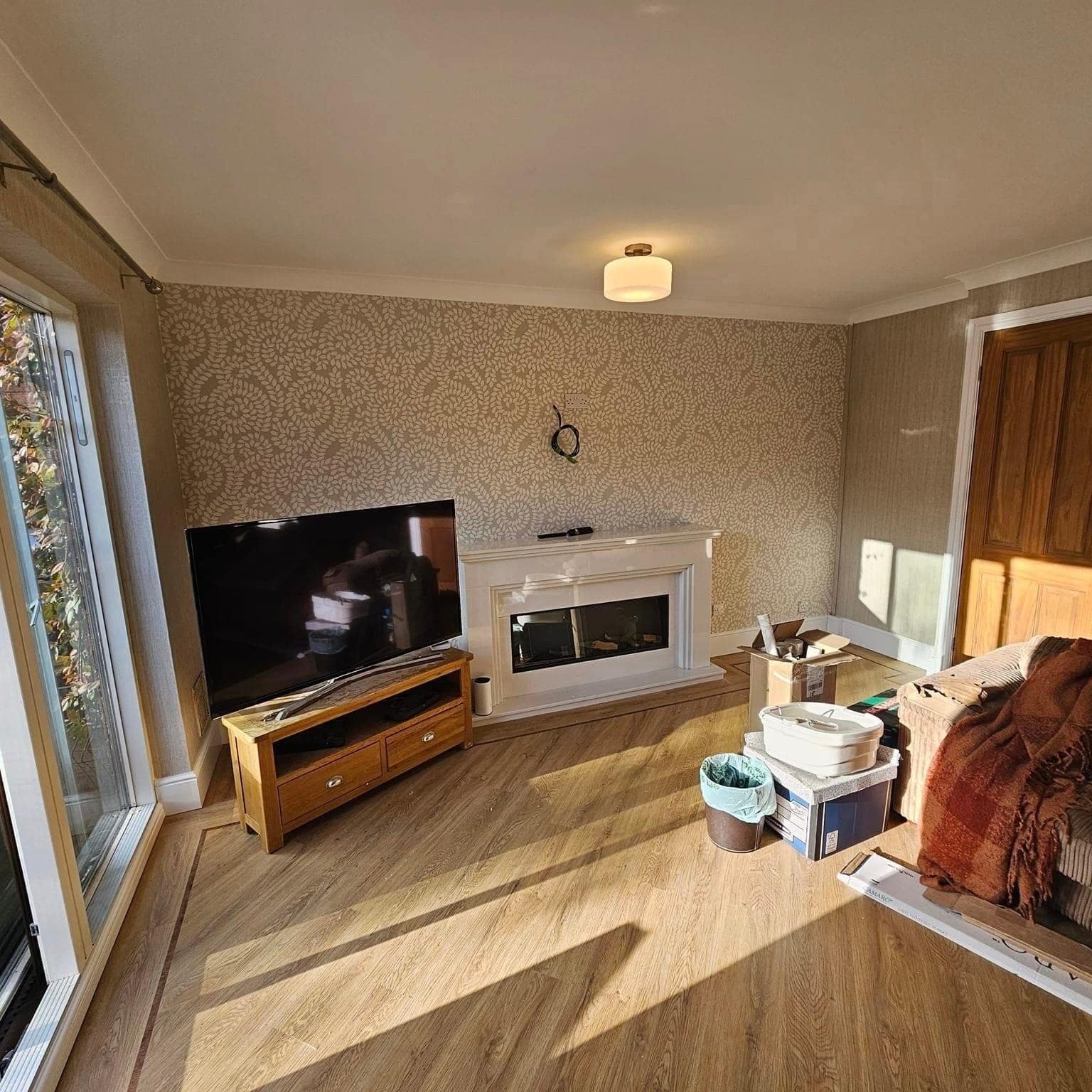 A bright lounge papered in a textured neutral wallcovering, with wood flooring and a white fireplace