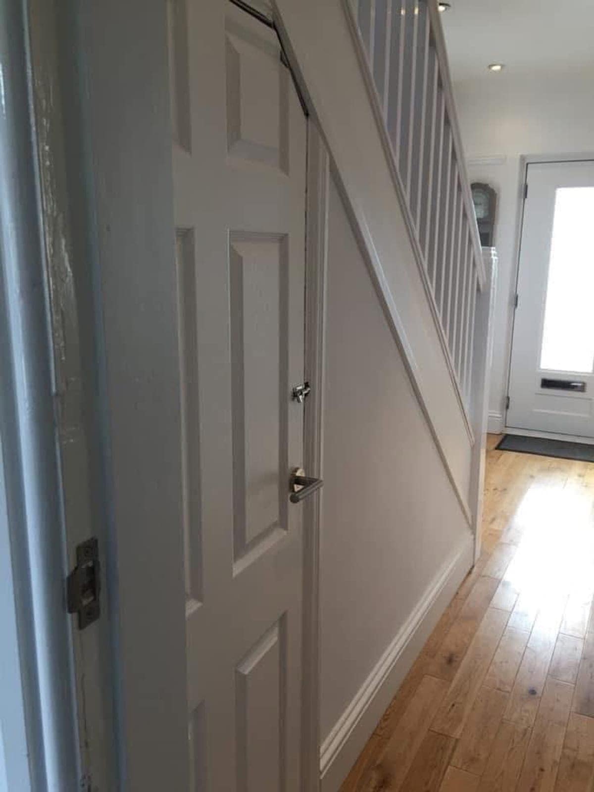 Finished hallway with the staircase painted white, oak floor and front door beyond